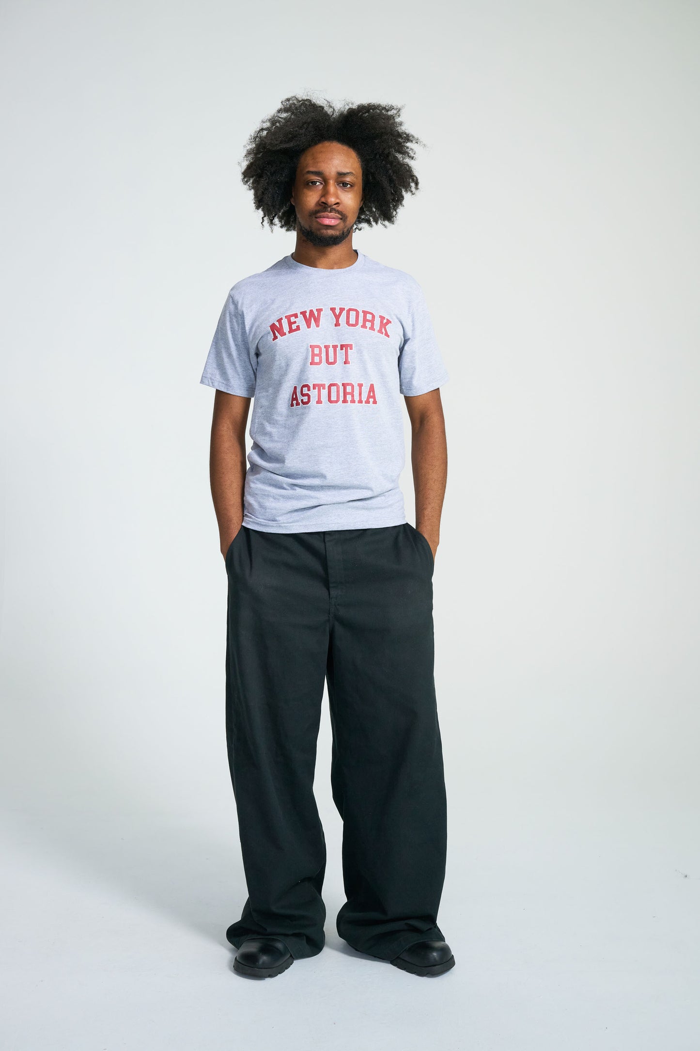 Person wearing a gray t-shirt with 'New York But Astoria' text on a white background