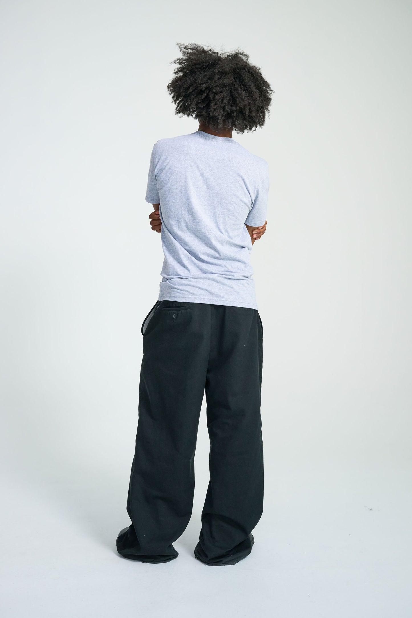 Person wearing a light gray t-shirt and dark pants on a white background