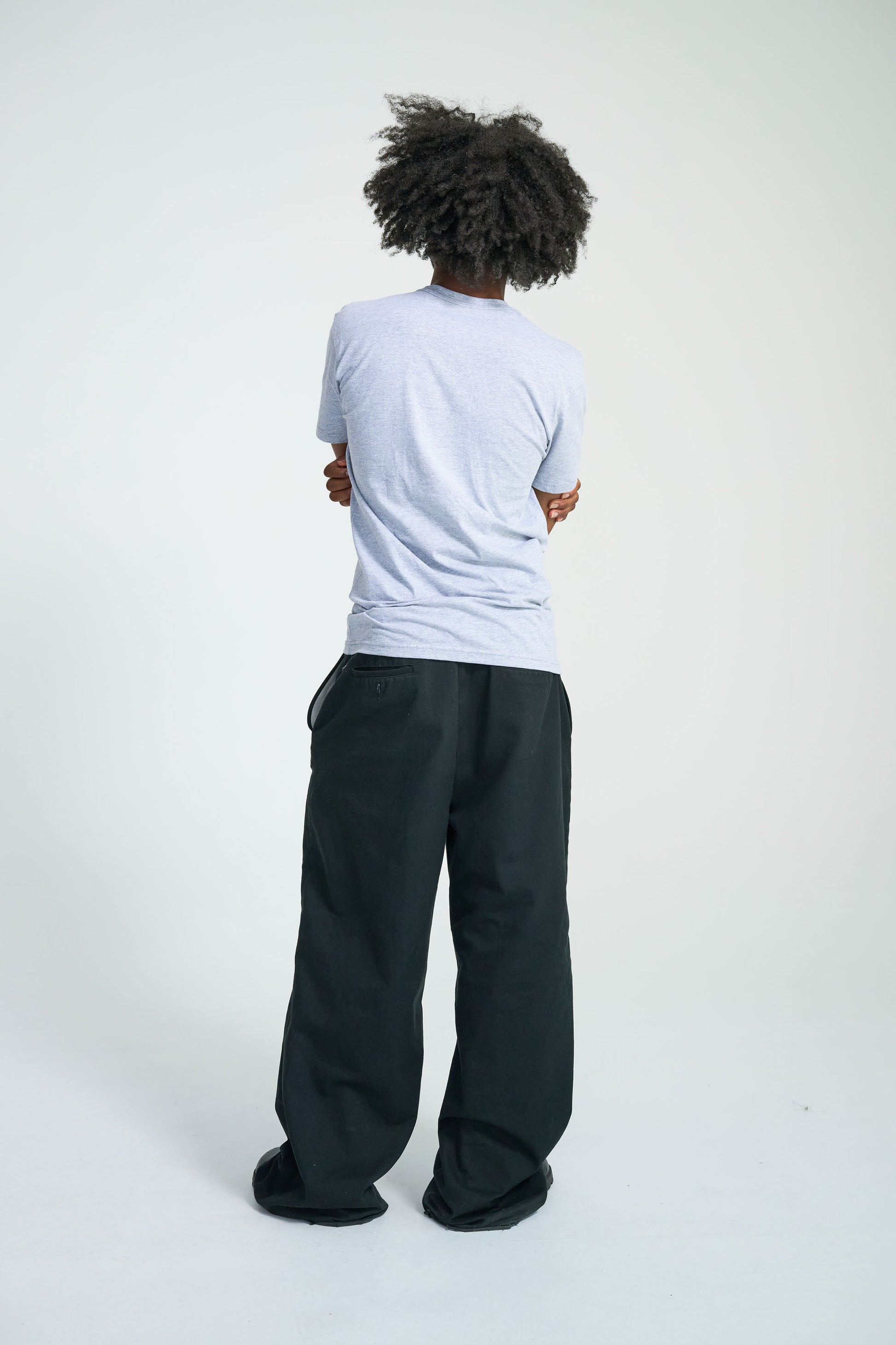 Person wearing a light gray t-shirt and dark pants on a white background