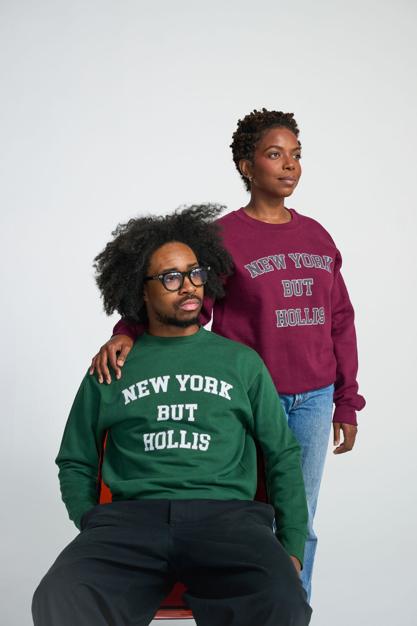 Two people wearing sweatshirts with 'New York But Hollis' text on a plain background