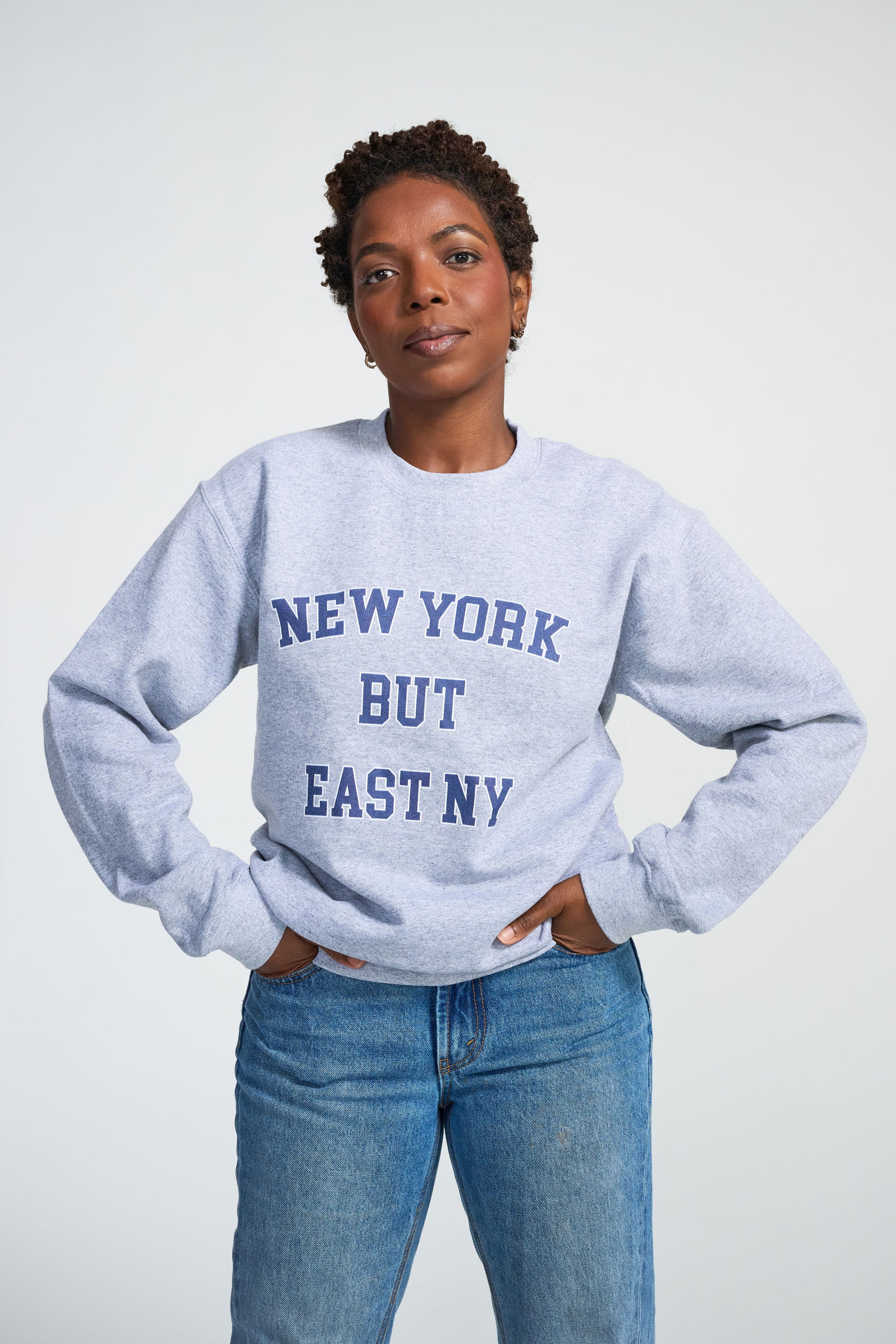 Person wearing a light blue sweatshirt with 'New York But East NY' text on a white background
