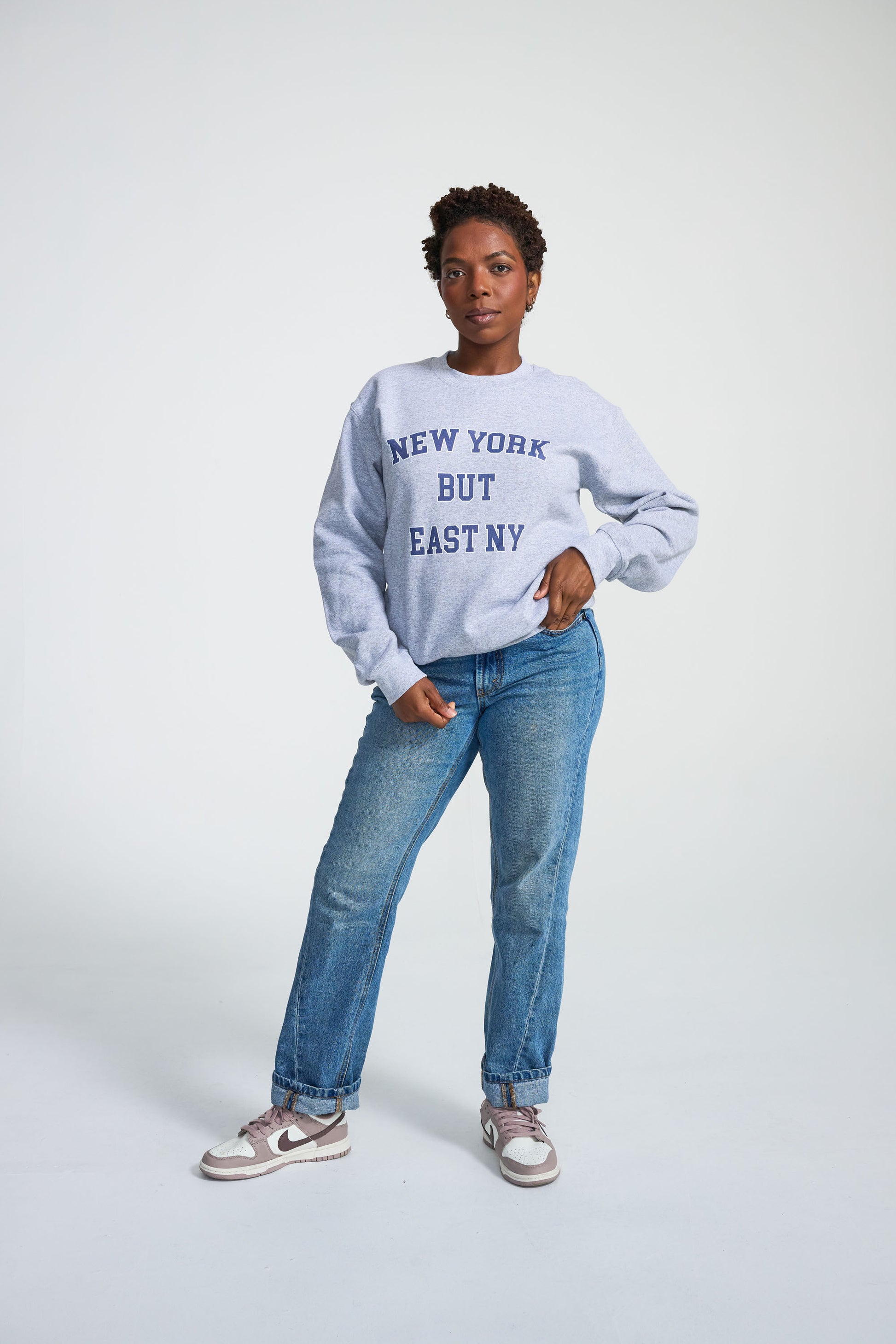 Person wearing a light blue sweatshirt with text and blue jeans on a white background