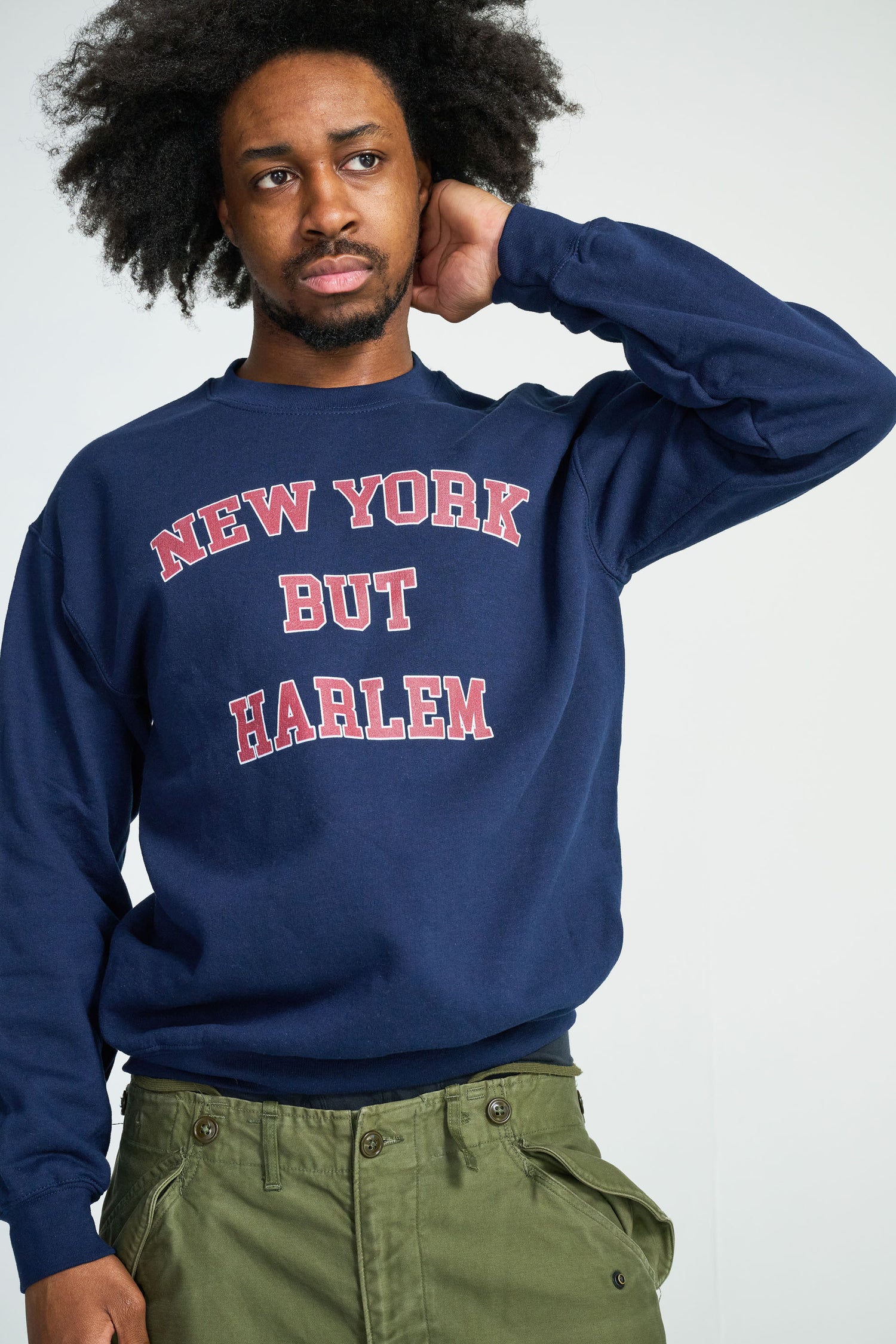 Person wearing a navy blue sweatshirt with 'New York But Harlem' text on a white background