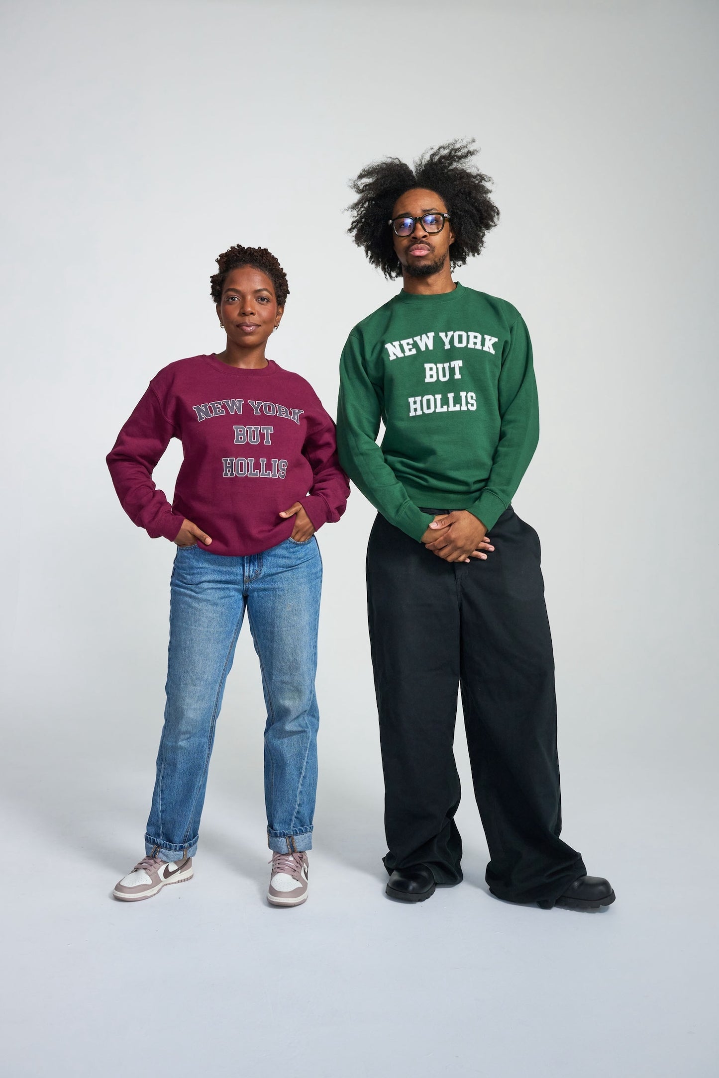 Two people wearing sweatshirts with text, standing against a plain background